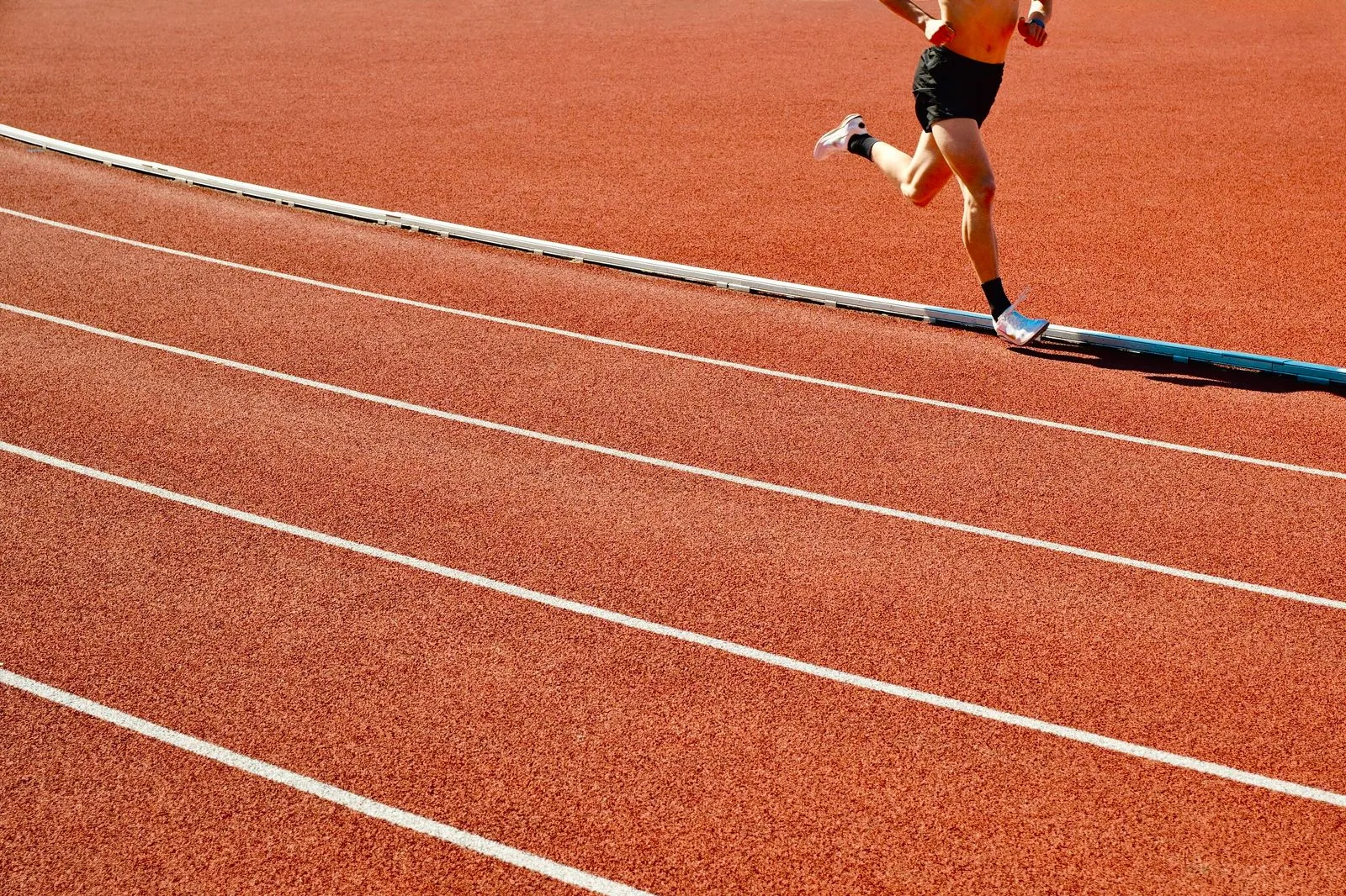 Athlete running on a red track in an outdoor stadium on a sunny day