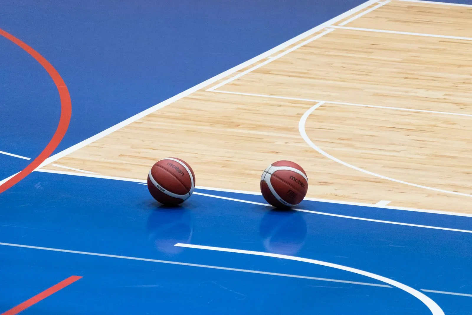 Two basketballs resting on a blue indoor basketball court